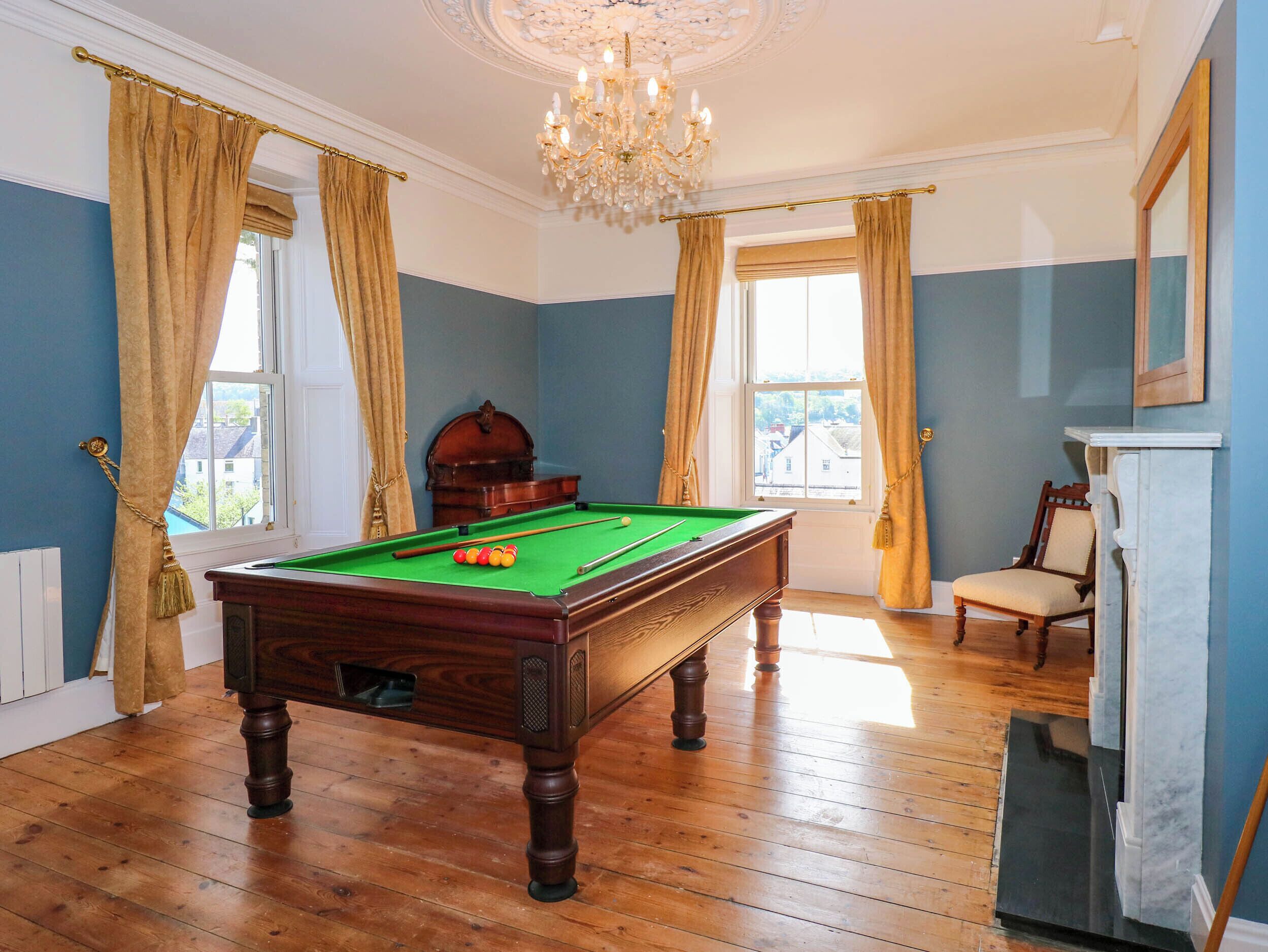 A billiards room with a pool table, a wooden cabinet, a chair, and a fireplace.