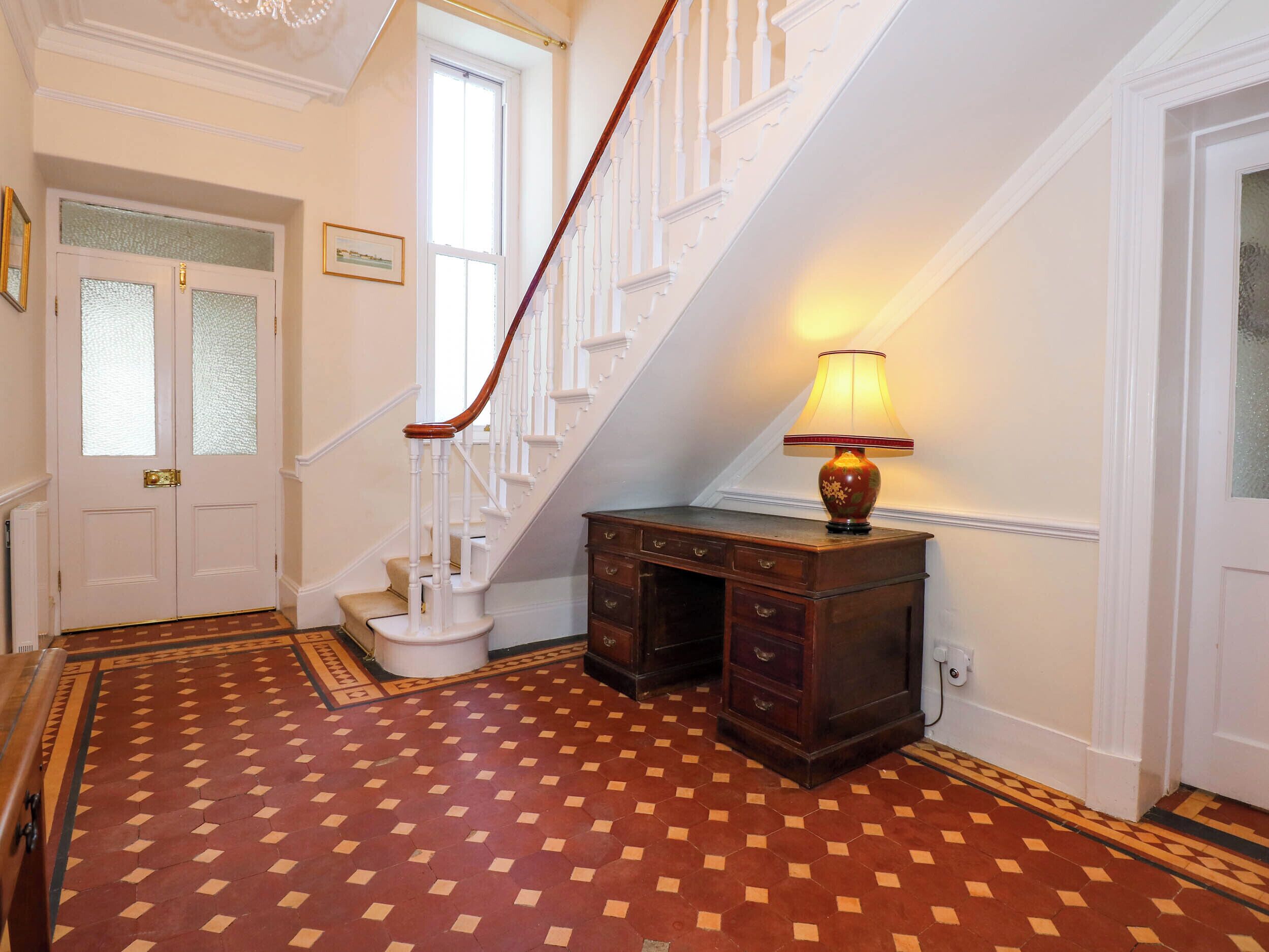 A staircase with white balusters, a wooden desk with drawers, and a patterned floor.