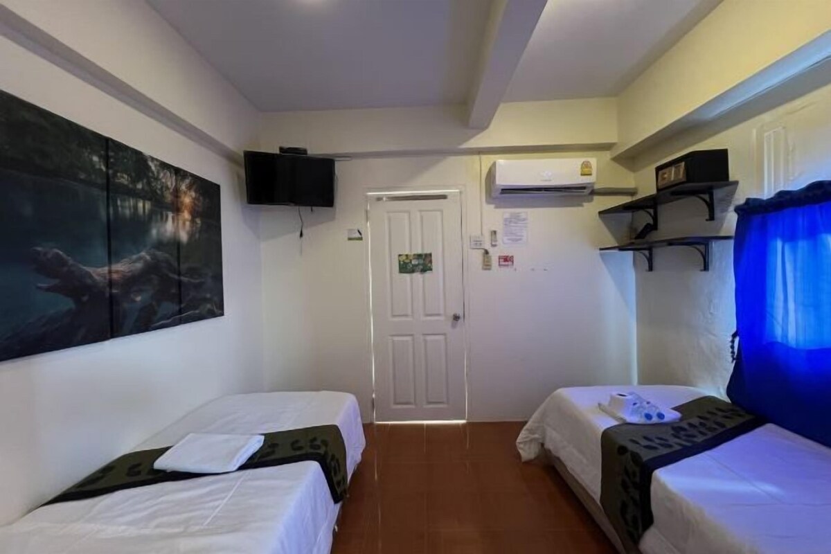 Une chambre avec deux lits, un téléviseur fixé au mur, un appareil de climatisation et une porte.