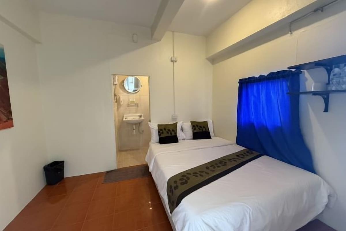 Une chambre à coucher avec un lit, une table de chevet, un miroir et une salle de bain visible à travers une porte ouverte.
