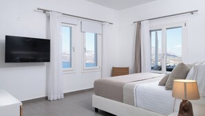 A modern bedroom with a bed, a TV, and large windows with curtains. - Zen Villas (Akrotiri)