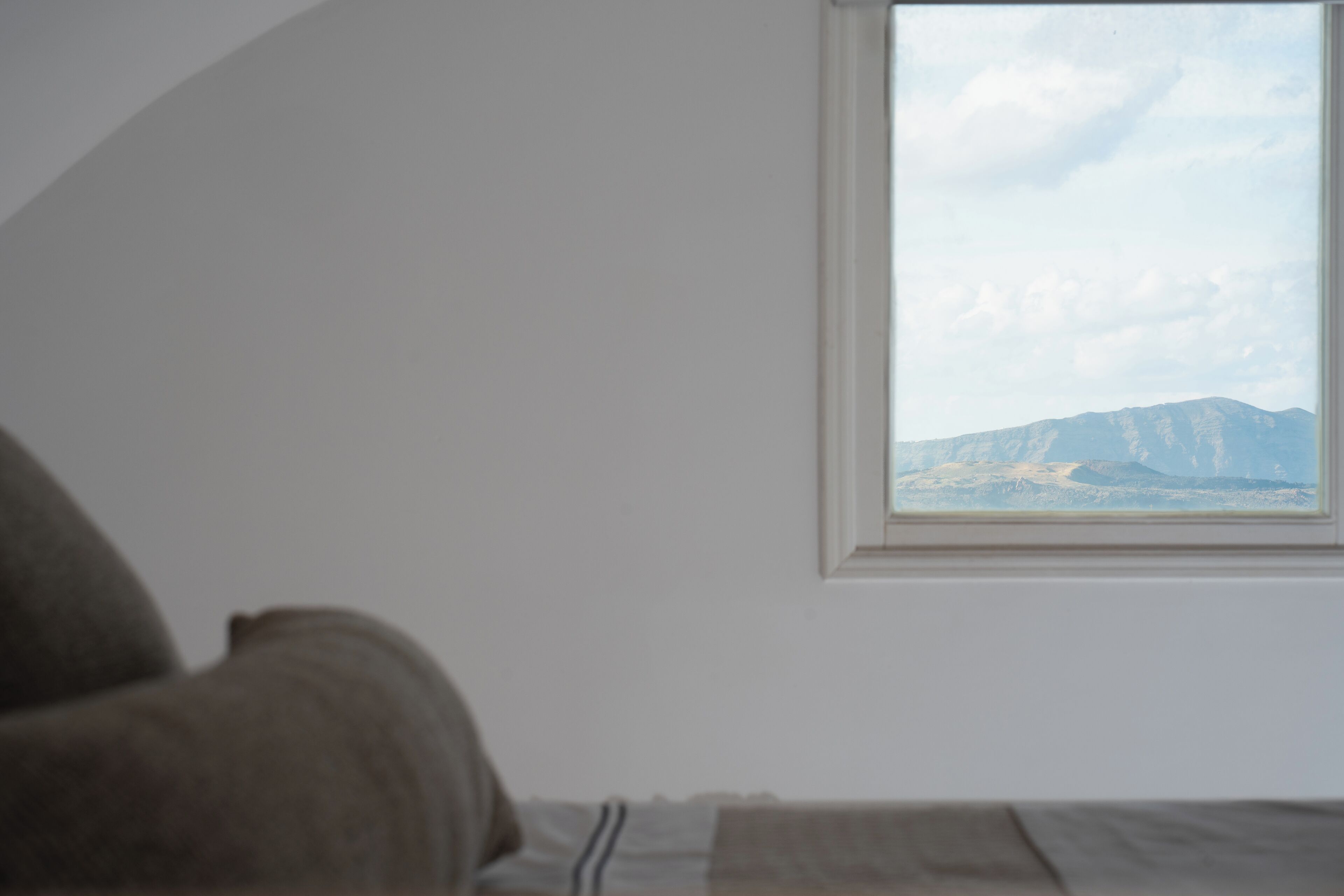 Una stanza con un letto, una finestra vista montagna e una porzione di parete.