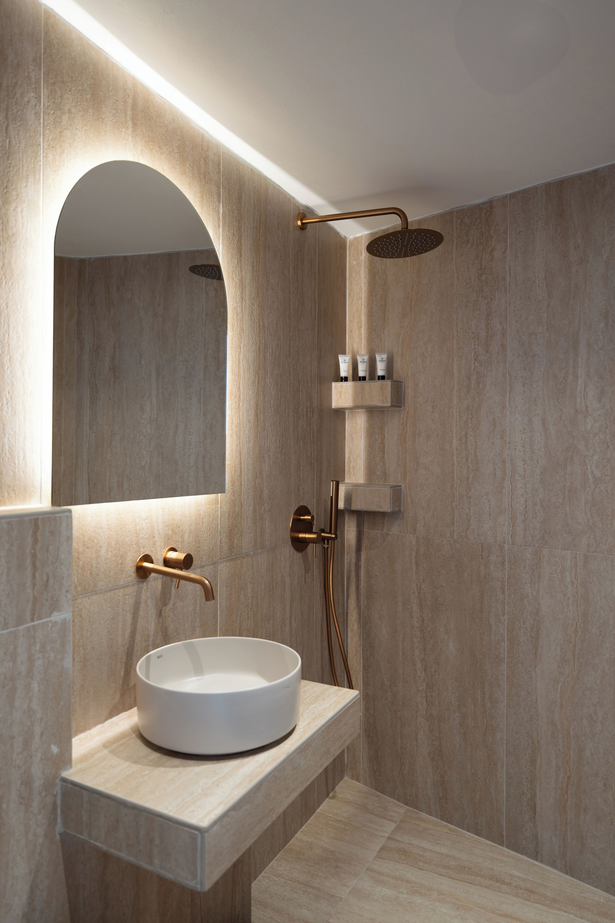 Un baño moderno con un lavabo redondo, un espejo y una ducha con cabezal de ducha manual.