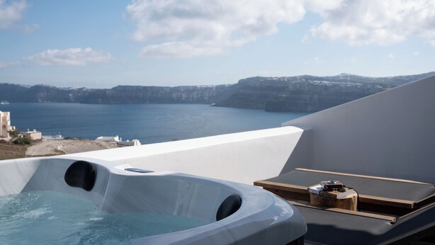 A hot tub with a view of the sea and cliffs, a lounge area with a table and chairs, and a clear sky. - Zen Villas (Akrotiri)