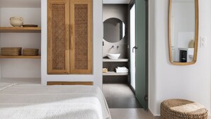 Une chambre à coucher comprenant un lit, des étagères en bois, un panneau en rotin, un miroir, et une salle de bain avec un lavabo et un porte-serviettes.