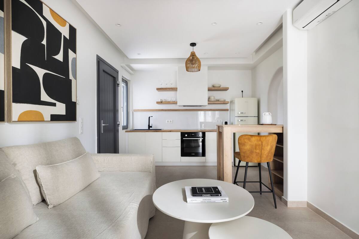 A modern living room with a sofa, a coffee table, and a dining area with a kitchen in the background.