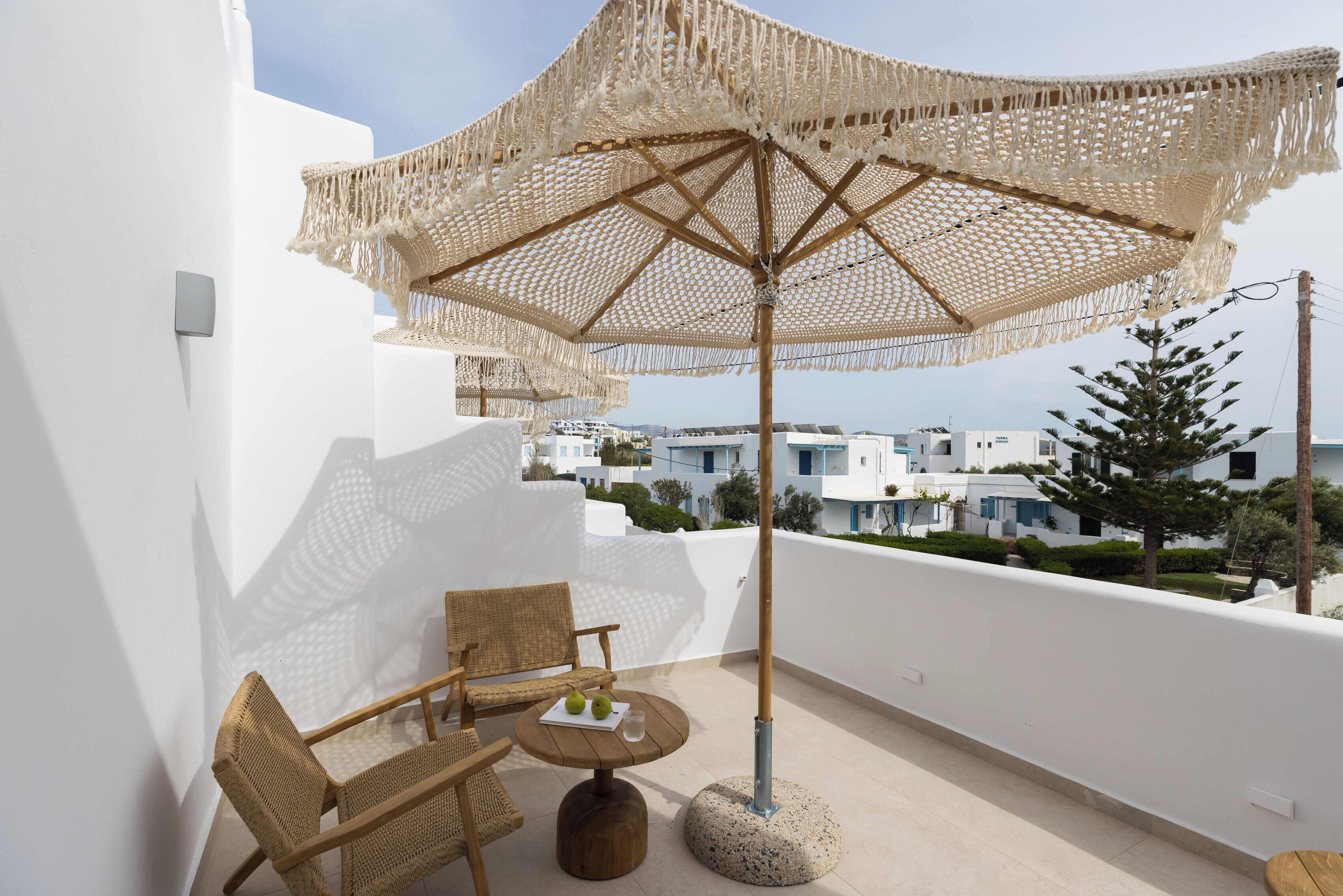 A balcony with wicker furniture, a round table with a plate and a glass, and a large woven umbrella.