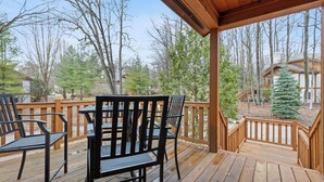 Una terraza de madera con mobiliario exterior y vistas a un bosque y una cabaña.