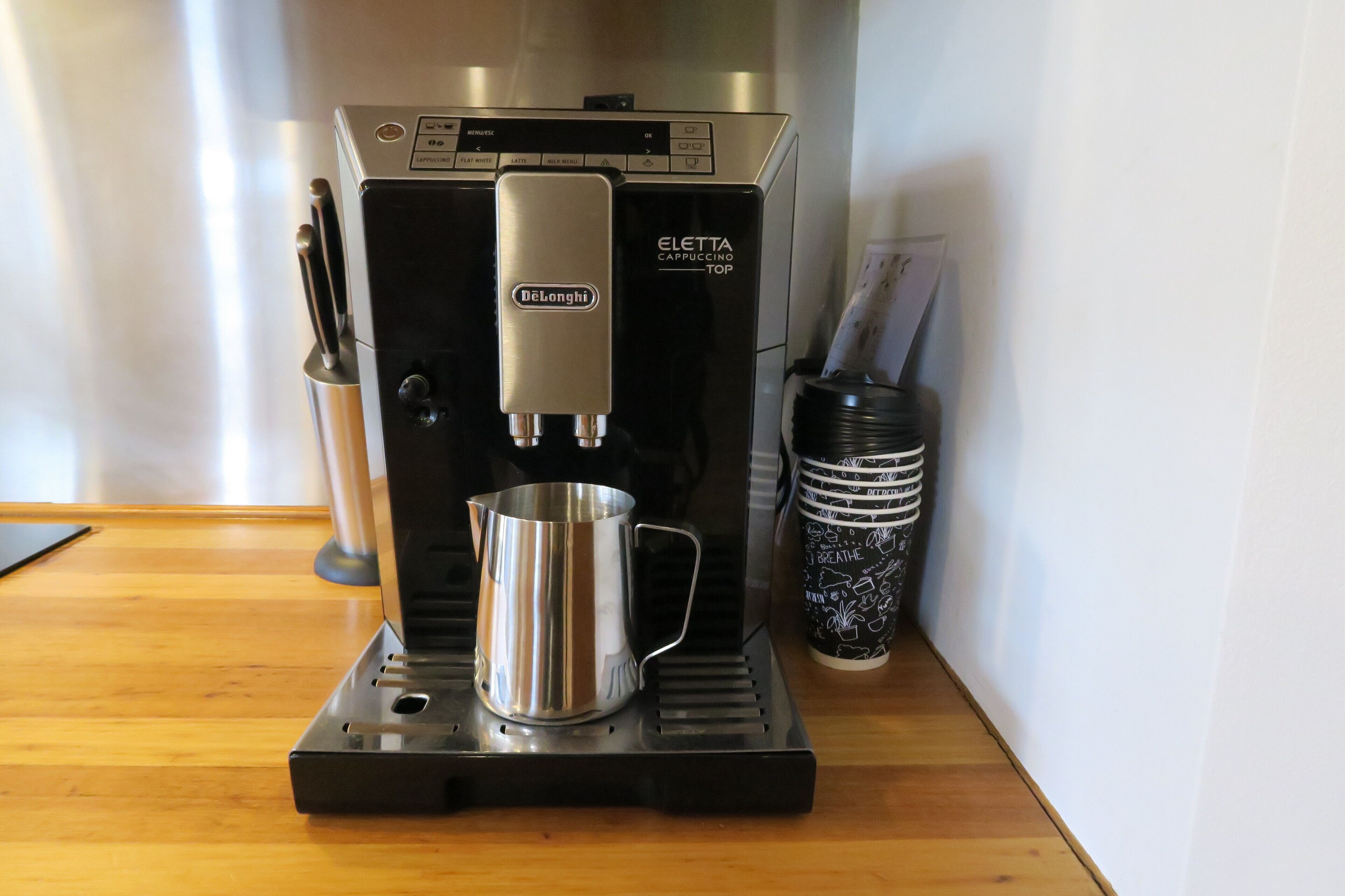 Una cafetera De'Longhi Eletta Cappuccino Top sobre una encimera de madera.