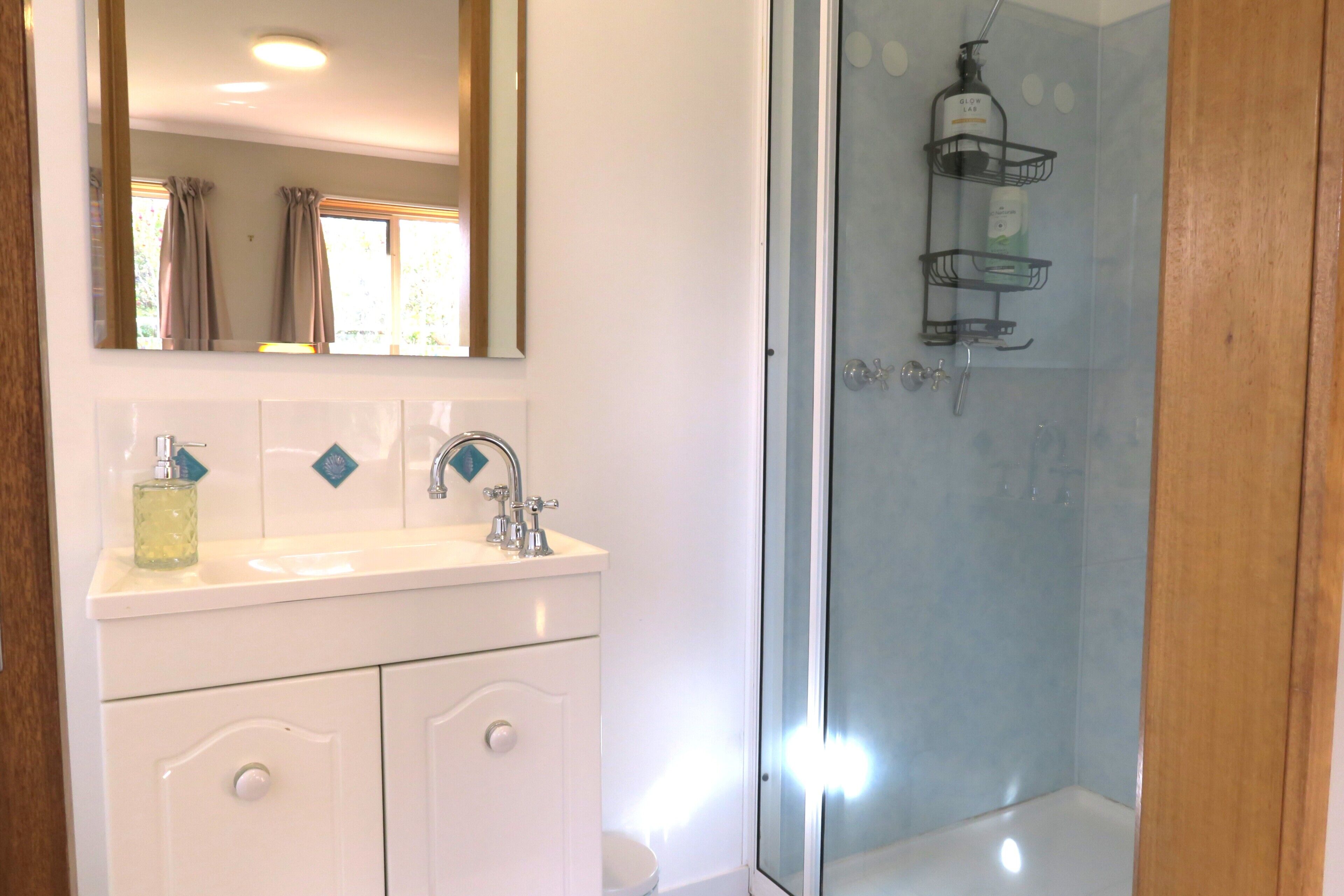 A bathroom with a white vanity, a mirror, a glass shower enclosure, and a window with curtains.