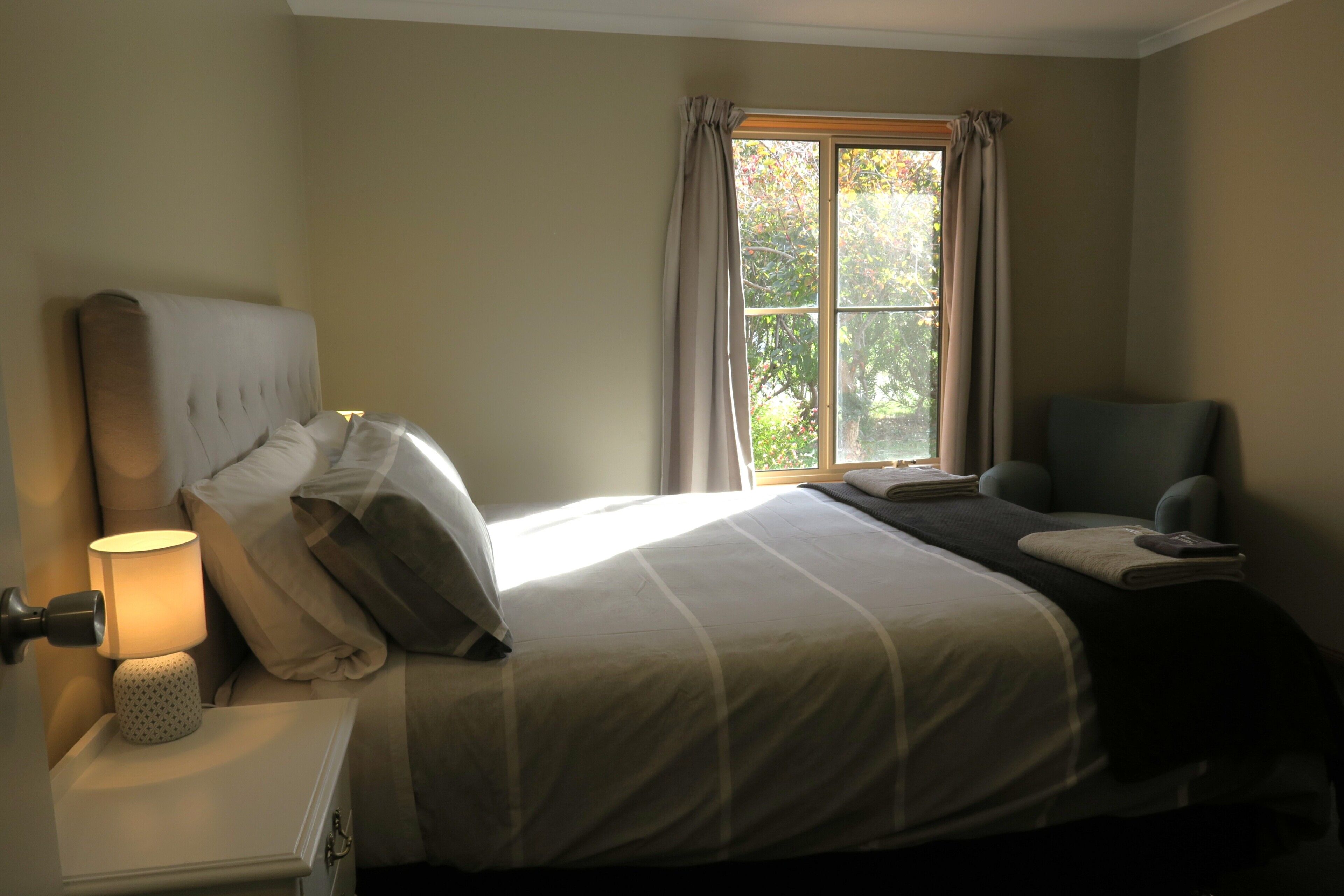 A neatly made bed with a headboard, a bedside lamp, and a chair.