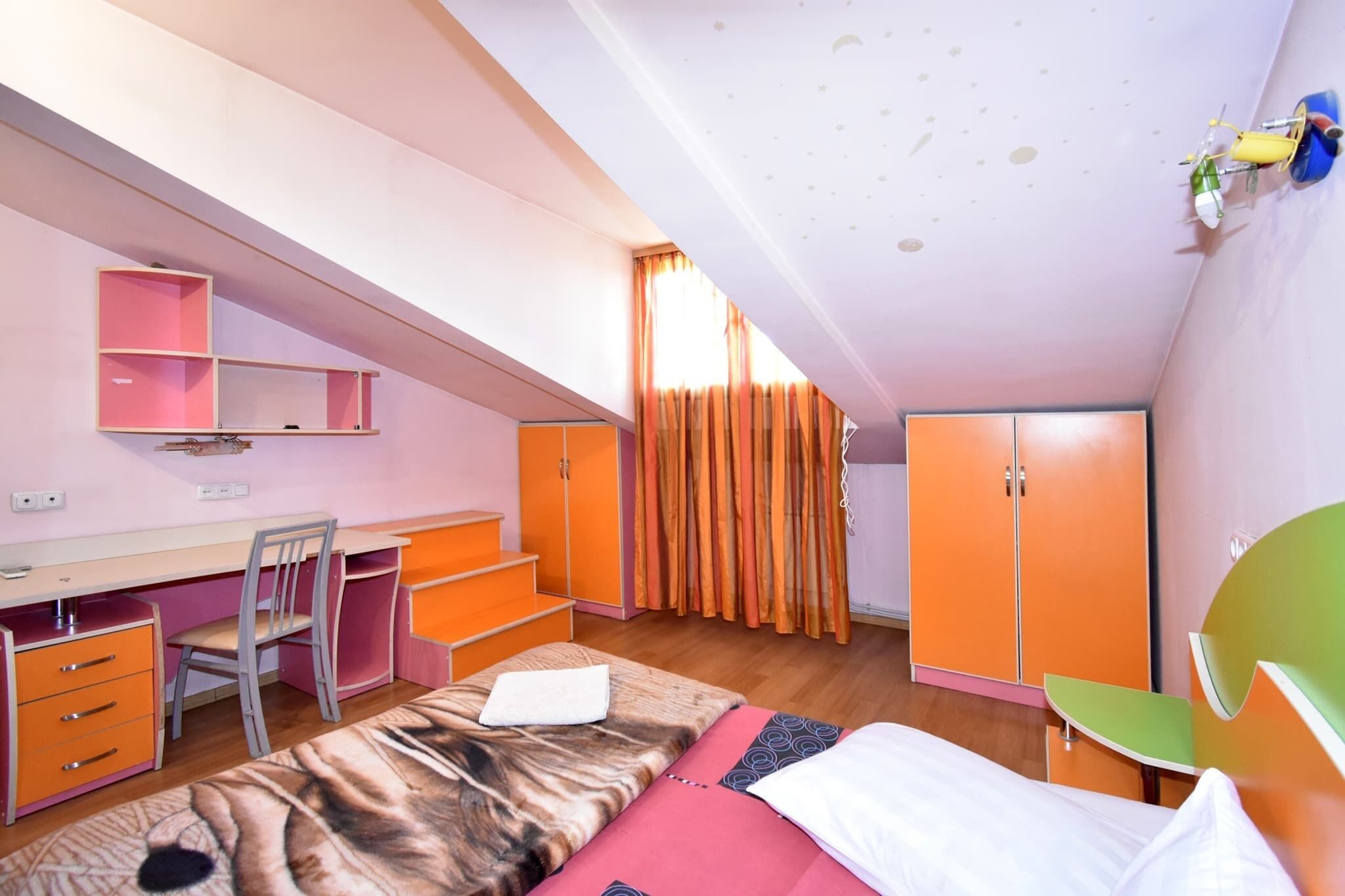A bedroom with a bed, desk, chair, wardrobe, and a window with curtains.