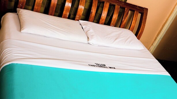 A bed with a white and teal bedspread and a wooden headboard. - Kisumu Travelers Hotel (Kisumu)