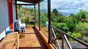 Ein überdachter Balkon mit Holzboden, einem Tisch, einer Flasche und einem Stuhl.