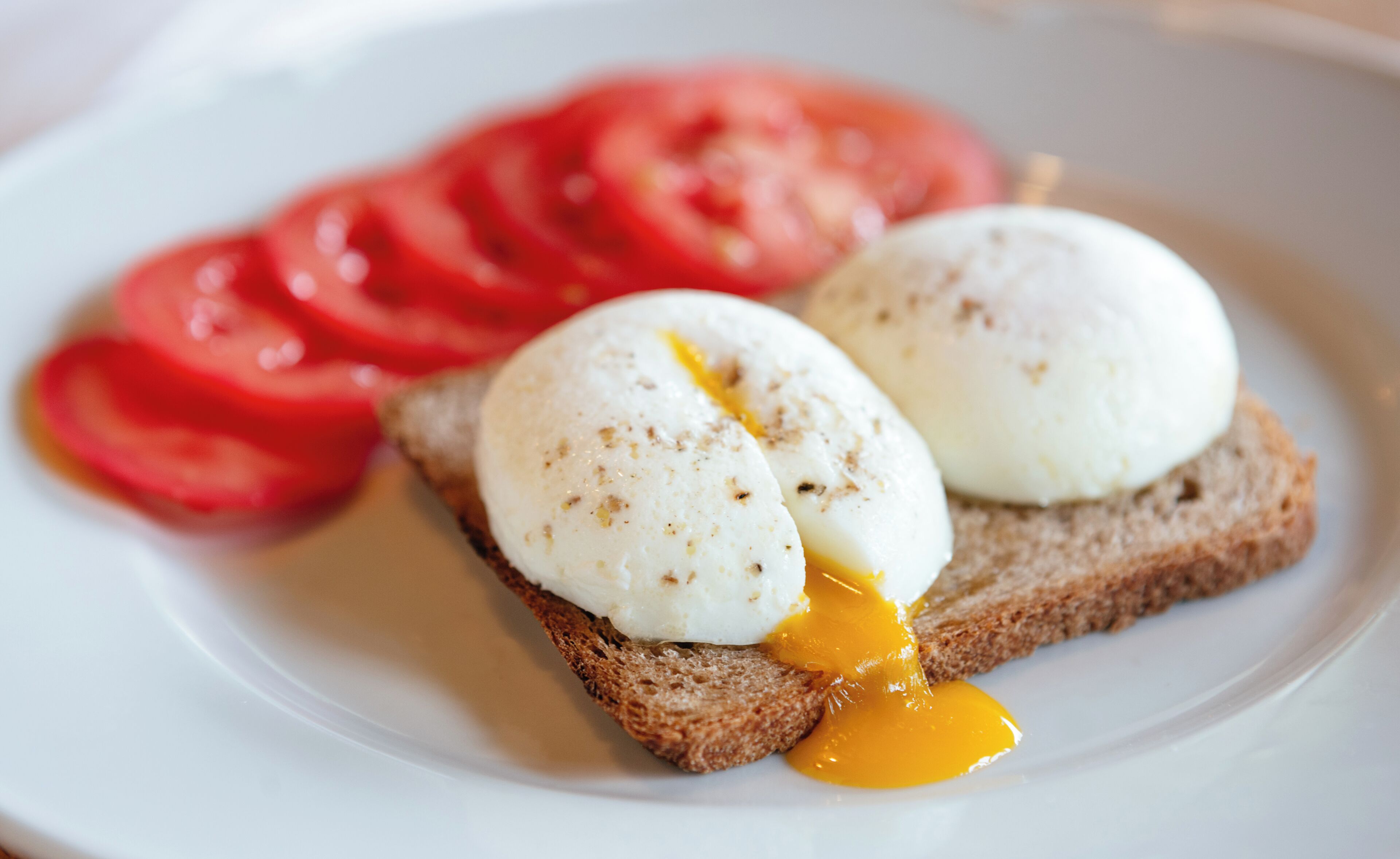 Un plato con dos huevos pochados sobre tostadas y rodajas de tomate.