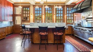 A kitchen with a large island, bar stools, a stove, and a large window with multiple panes. - Little Daisy Jerome Historic Mansion Sedona Views (Sedona)
