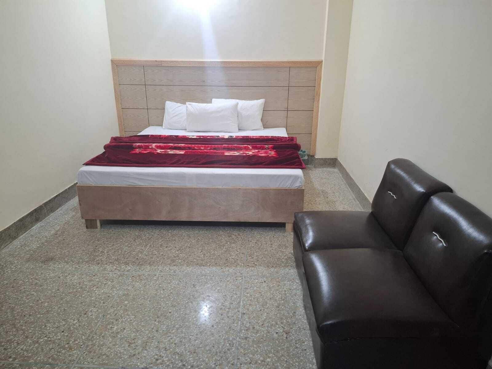 Un dormitorio con cama, cabecera, manta roja y sillón de cuero.