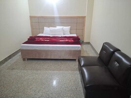 A bedroom with a bed, a headboard, a red blanket, and a leather chair.