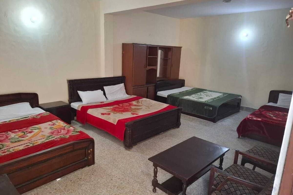 Una habitación con dos camas, un armario de madera, una mesita pequeña y una maleta verde.