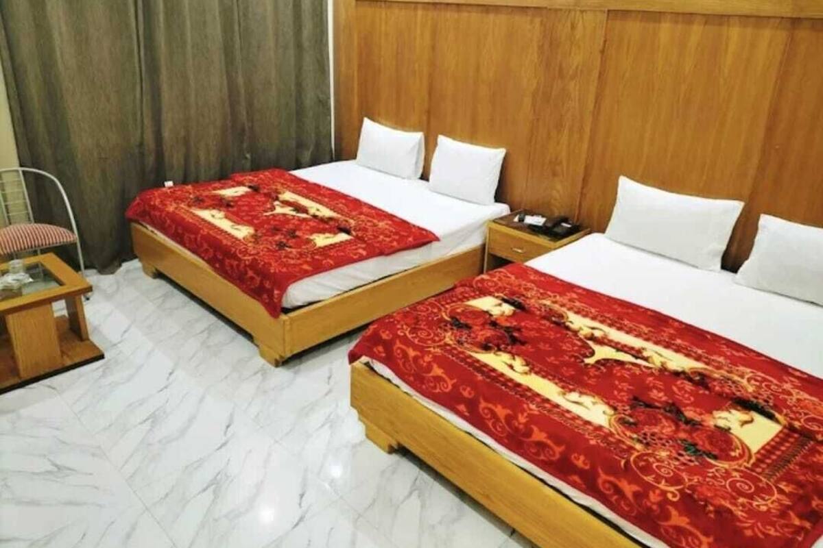 Habitación de hotel con dos camas, cada una con una colcha de diseño rojo y dorado, almohadas blancas y cabeceros de madera.