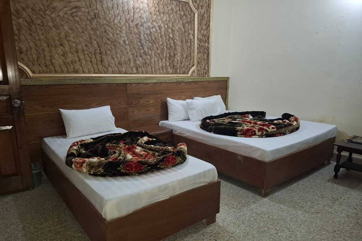 Dos camas individuales con cabeceros de madera, ropa de cama blanca y mantas estampadas con motivos florales.