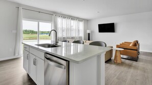 A modern kitchen with a large island, a dining area with a sofa and chairs, and a TV mounted on the wall. - 4 BR Beauty-Millville by the Sea~ Minutes to Bethany Beach -23548 Bonfire Way (Millville)