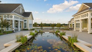 A building with a pond in the center, surrounded by a walkway and greenery. - 4 BR Beauty-Millville by the Sea~ Minutes to Bethany Beach -23548 Bonfire Way (Millville)