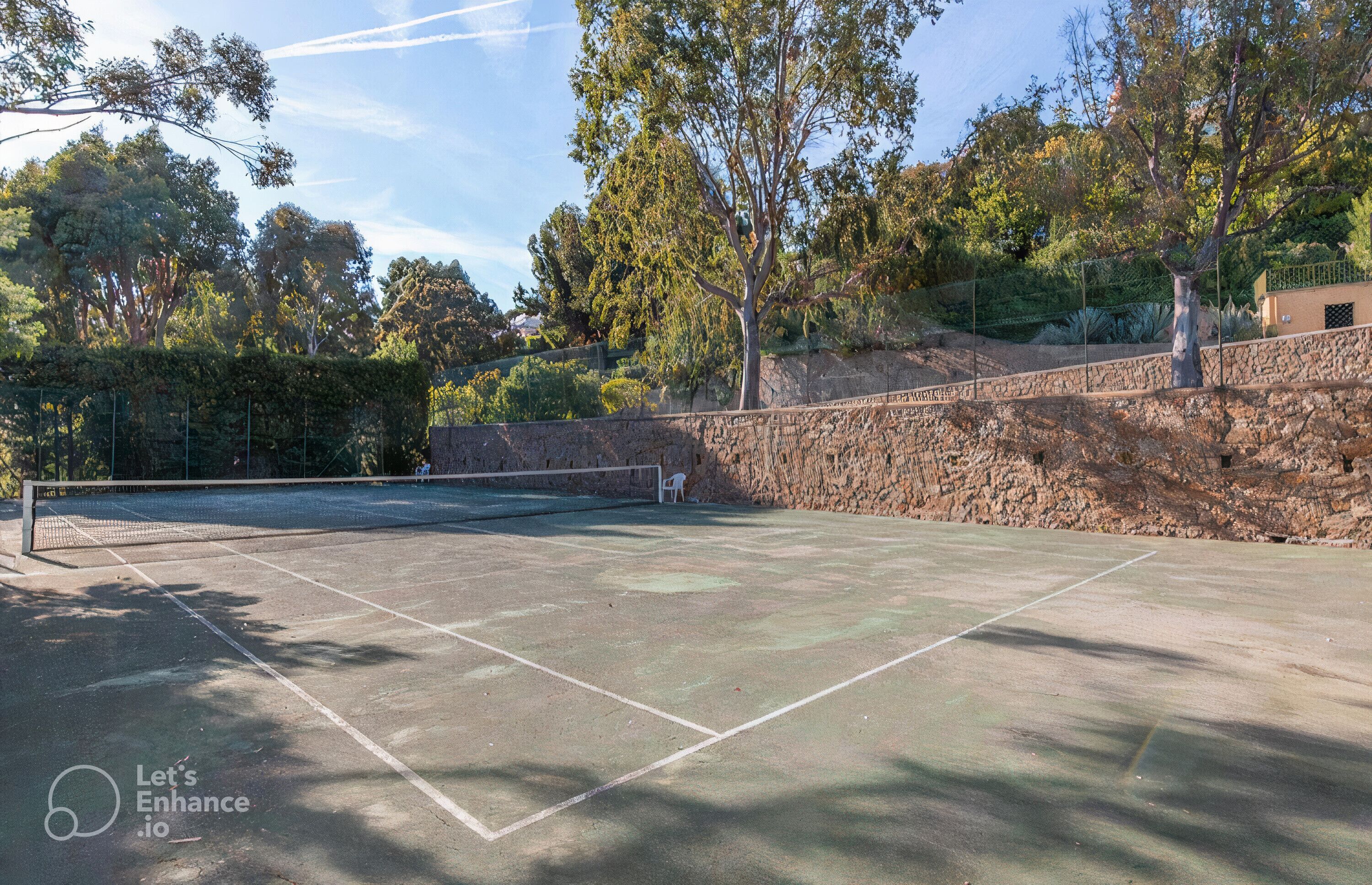 An outdoor tennis court with a stone wall and trees in the background.