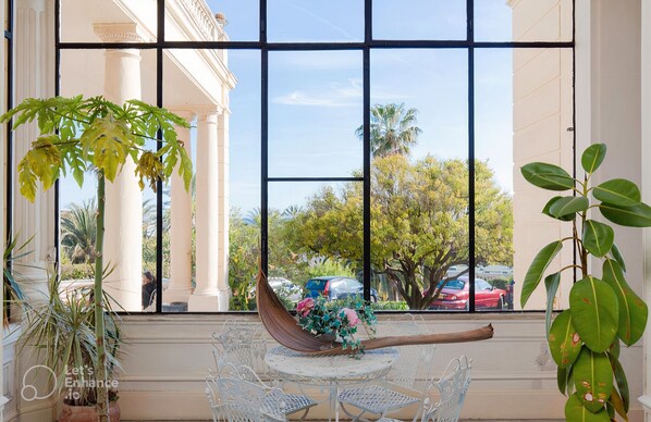 A room with a large window, a hammock, and a table with chairs.