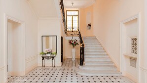 Een statige trap met een zwarte ijzeren balustrade, een witte muur met decoratieve sierlijsten en een betegelde vloer met een ruitmotief.