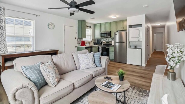 A modern living room with a beige sofa, a ceiling fan, and a kitchen in the background. - Fully Furnished 2BR Near Duke & VA Hospital Ideal for Medical & Extended Stays (Durham)