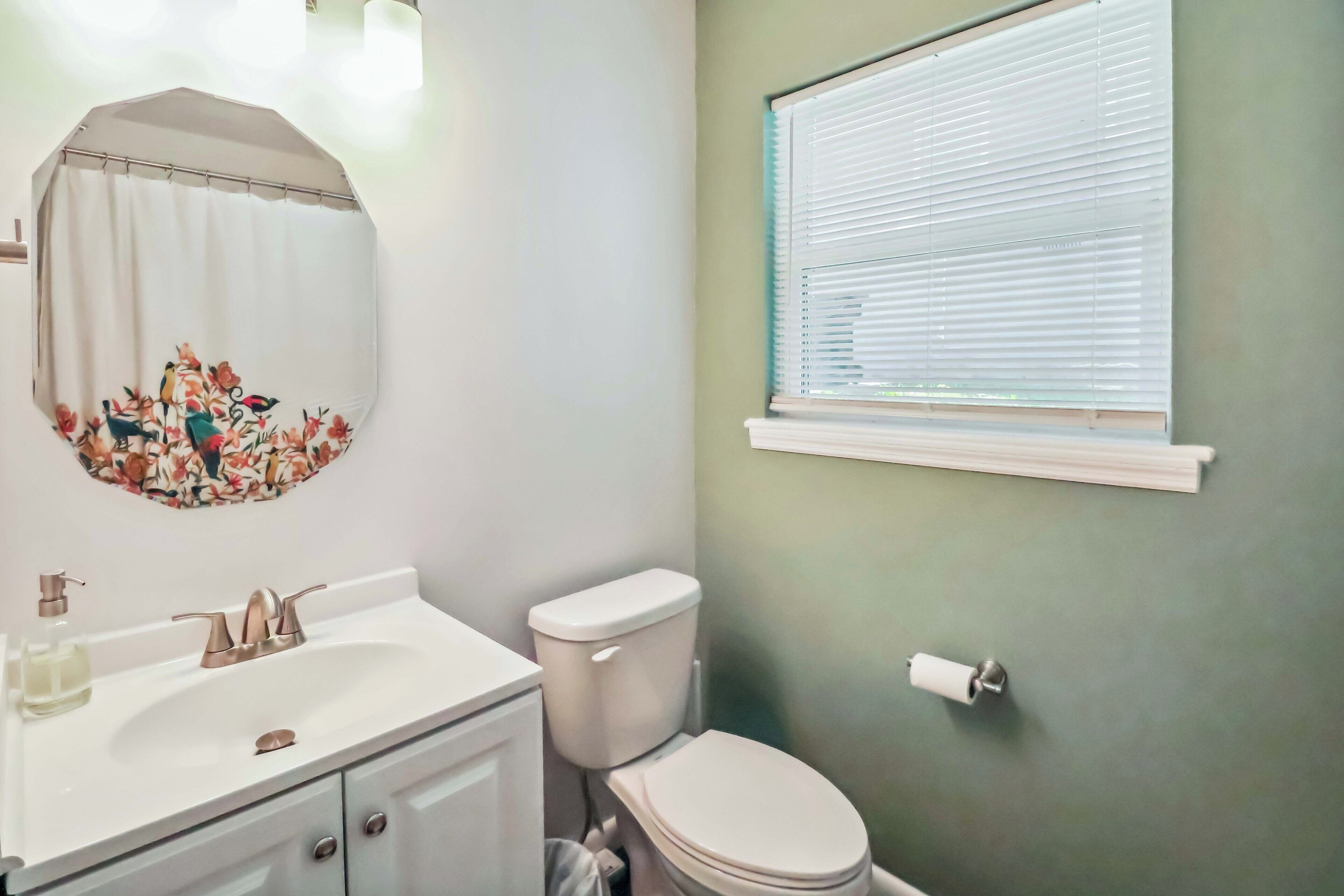 Un baño con lavamanos blanco, inodoro y ventana con persianas.