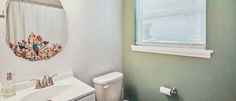 Un baño con lavamanos blanco, inodoro y ventana con persianas.