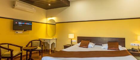 A hotel room with a bed, a desk, two chairs, a TV, and a lamp.