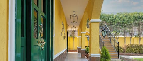 A corridor with patterned floor tiles, green doors, and a staircase leading to a garden area.