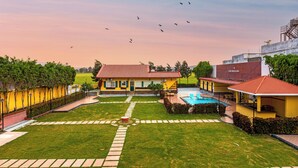 A yellow building with a swimming pool, surrounded by a well-maintained lawn and a clear sky. - Greenfields Resort (Bhopal)