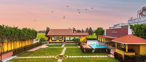 A yellow building with a swimming pool, surrounded by a well-maintained lawn and a clear sky.