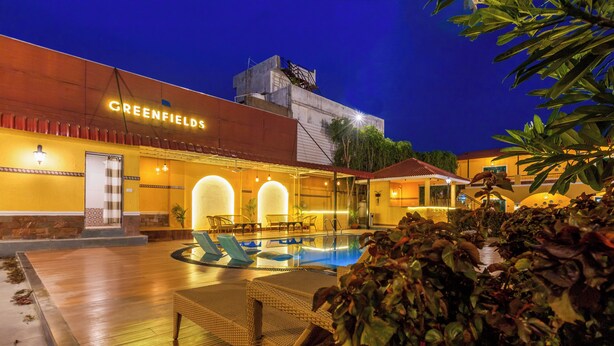 A hotel with a swimming pool, outdoor seating, and a well-lit entrance. - Greenfields Resort (Bhopal)