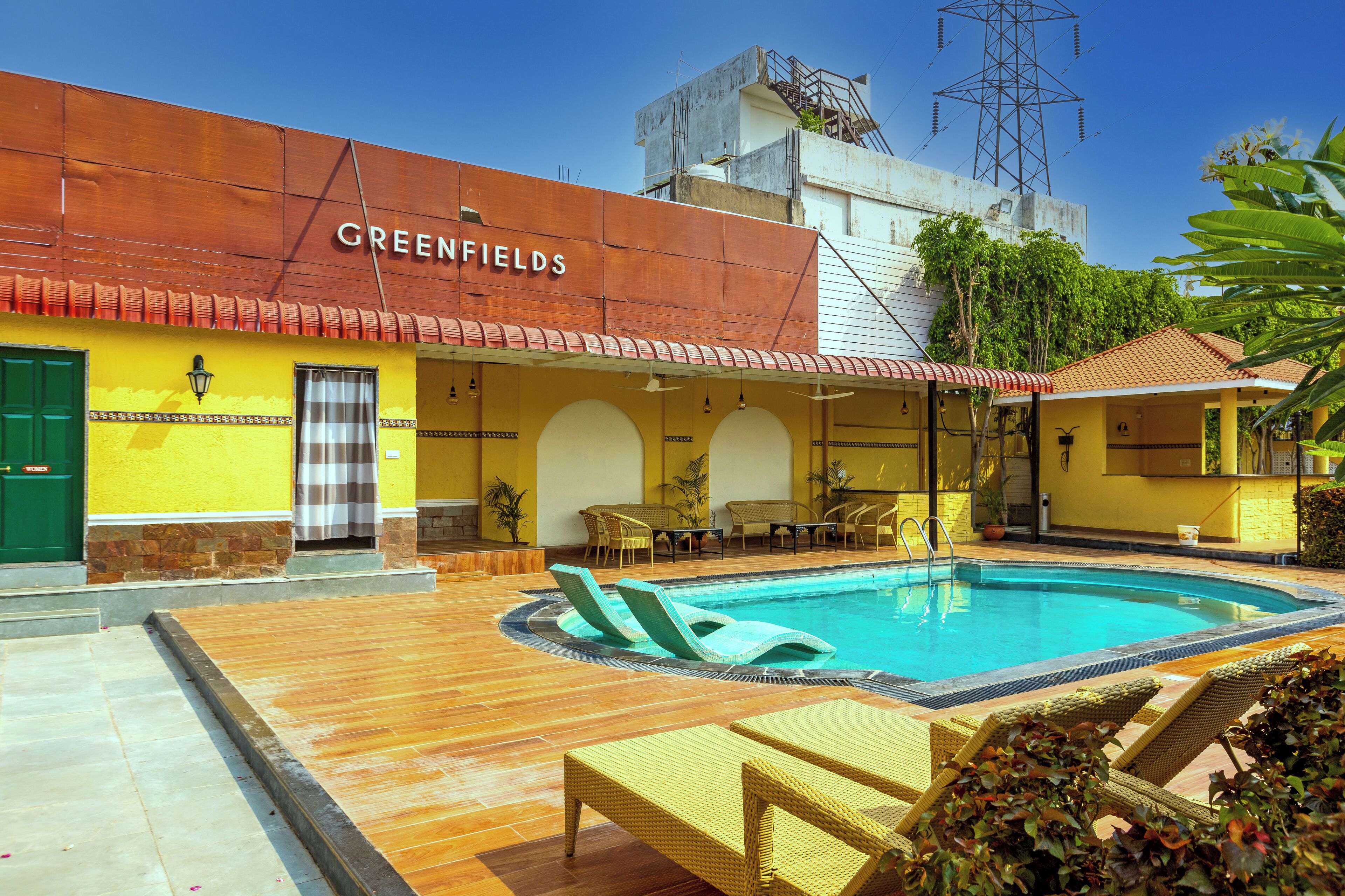 Un hotel llamado Greenfields con piscina, sillones de descanso y mobiliario exterior.