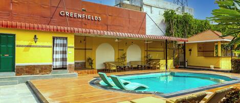 A hotel named Greenfields with a swimming pool, lounge chairs, and outdoor seating.