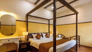 A four-poster bed with a wooden frame, a bedside table with a lamp, a chair, and a large mirror on the wall. - Greenfields Resort (Bhopal)