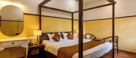 A four-poster bed with a wooden frame, a bedside table with a lamp, a chair, and a large mirror on the wall.