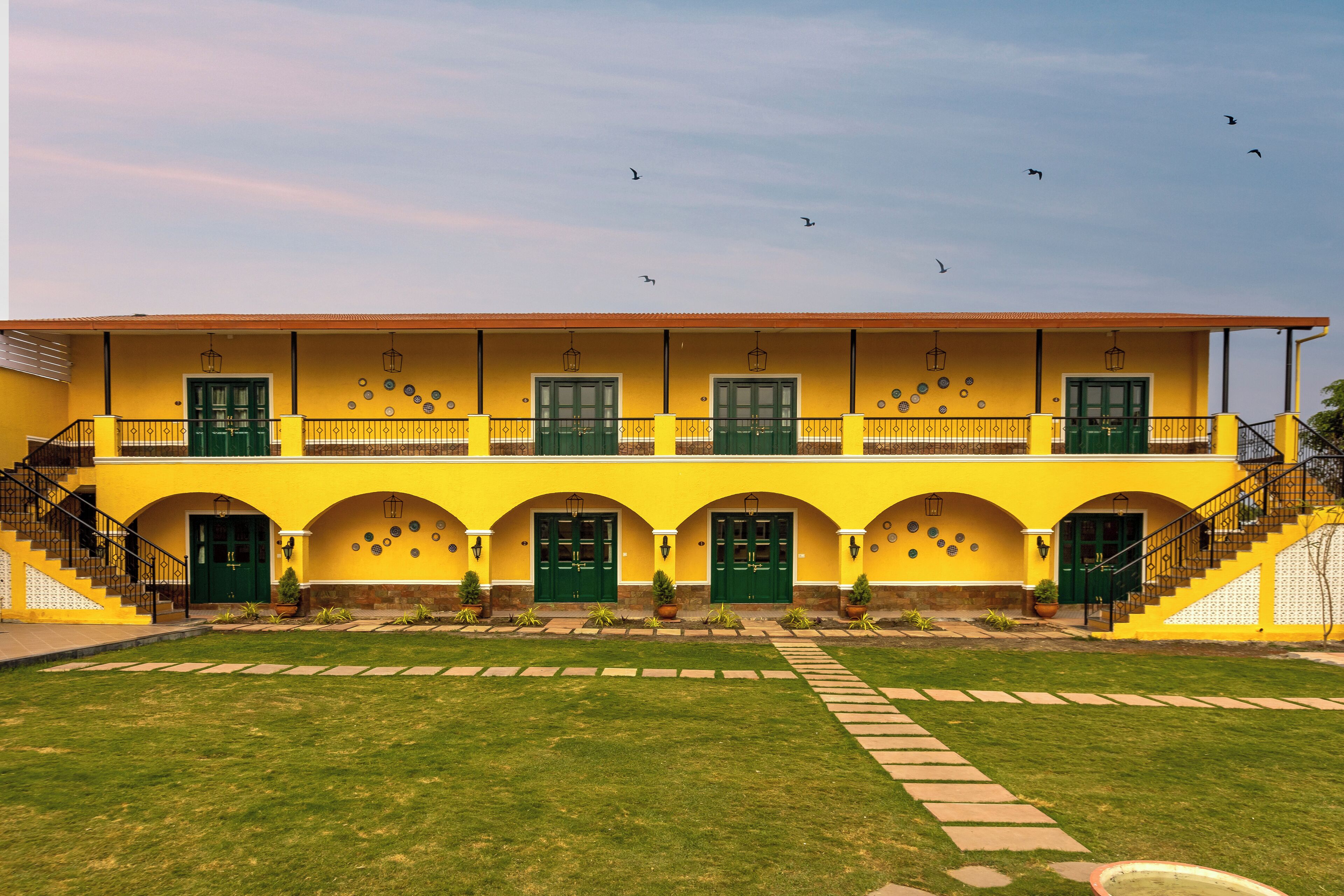 Un edificio amarillo con puertas y ventanas verdes, una escalera y un patio empedrado.