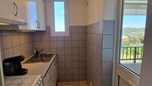 Una cocina compacta con ventana, estufa, lavamanos y cafetera.