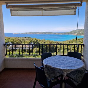 Un balcón con mesa y sillas, con vistas a la costa y un cielo despejado.