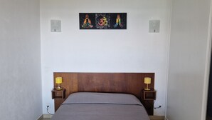 Un dormitorio con cabecera de madera, colcha gris, dos lámparas de noche y una obra de arte en la pared sobre la cama.