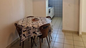 Un comedor con una mesa cubierta con un mantel estampado, sillas, un equipo de aire acondicionado y un televisor montado en la pared.