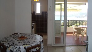 Una habitación con mesa de comedor, sillas, zona de cocina y puerta corrediza de vidrio que da a un balcón exterior con sillas.