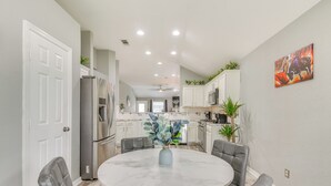 Una cocina moderna con armarios blancos, un refrigerador de acero inoxidable y un comedor con una mesa de mármol y sillas de cuero.