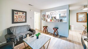 A living room with a sofa, a coffee table, and a dining area with stools. There is a kitchen area with a refrigerator and a sink. - 9 Mi to Dtwn Dallas: Cozy Couple's Getaway (Dallas)
